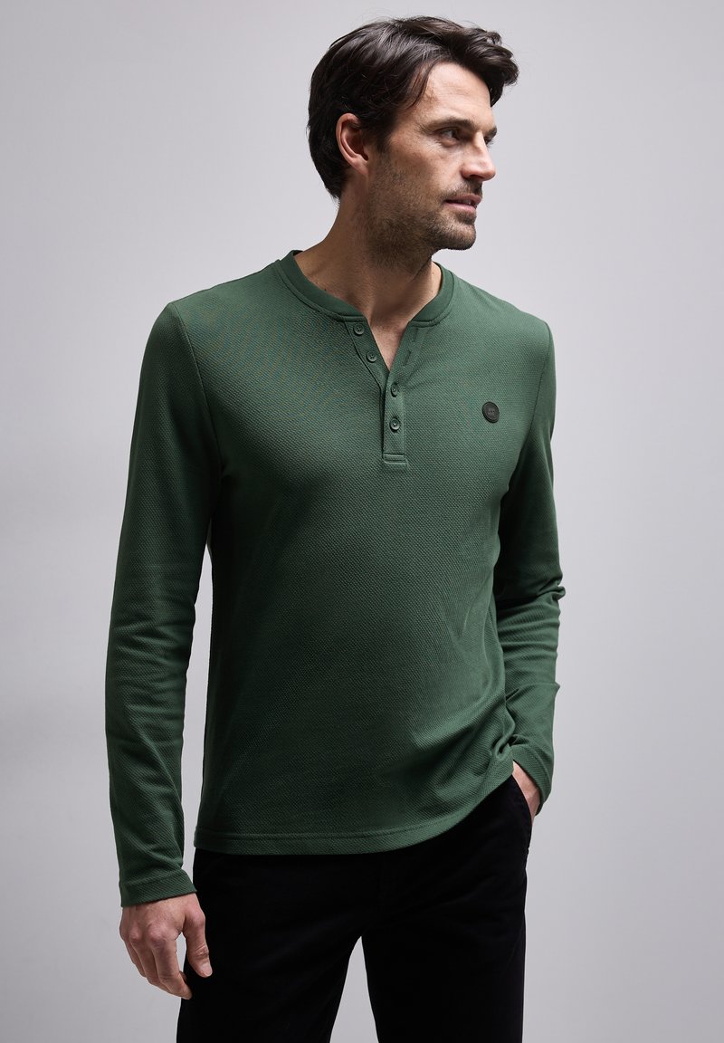 Grünes Langarm-Henley-Shirt aus strukturiertem Stoff, mit rundem Ausschnitt, einer Knopfleiste mit drei Knöpfen und einem kleinen schwarzen Logo auf der Brust.