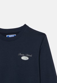 Σκούρα μπλε φούτερ κατασκευασμένο από μαλακό ύφασμα, με ριμπ λαιμόκοψη και λευκό κεντητό λογότυπο στο στήθος.