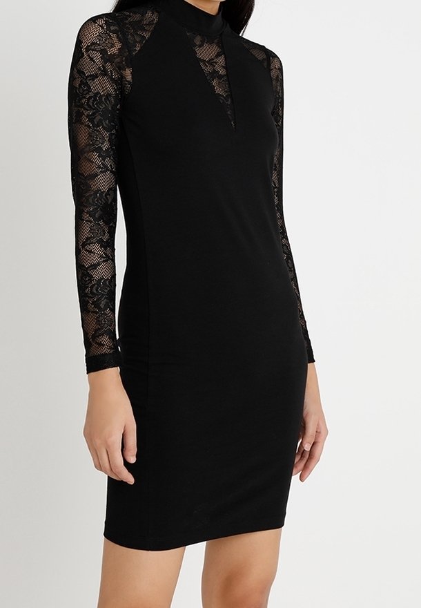 Femme portant une robe noire ajustée avec des manches longues en dentelle et un détail en dentelle en forme de V sur la poitrine.