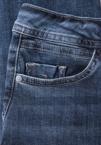 Jean en denim bleu foncé avec un design classique à cinq poches. Présente des coutures visibles et un détail en métal au niveau de la poche.