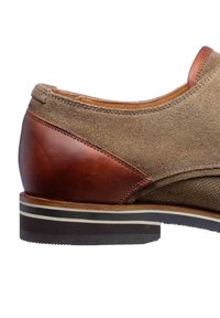 Bruine suède schoen met een donkerbruine leren hak. Heeft een gestructureerd oppervlak, contrasterende patronen en een witgestreepte zool.