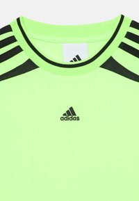 Žalia sportinė marškinė su juodomis juostelėmis, su raibomis tekstūra ir mažu juodu Adidas logotipu priekyje. Sukurtos su apvalia kaklo linija.