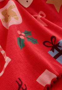 Rode stof met een gestructureerd oppervlak dat kerstthema patronen toont: peperkoekmannetjes, hulst, cadeaus en zuurstokken in verschillende kleuren.