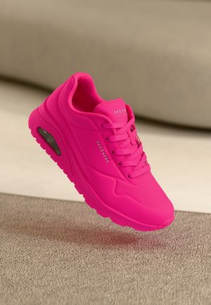 Jaskraworóżowy sneaker Skechers z grubą podeszwą i widoczną poduszką powietrzną, zasznurowany, pokazany pod kątem na neutralnym, dywanowym tle.