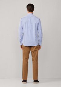 Camisa de botones a rayas azul claro y blanca con cuello, que presenta mangas largas y un dobladillo ligeramente curvado. Llevada con pantalones color beige.