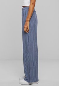 Pantalons larges à rayures bleues avec une taille élastique, en tissu léger, associés à des baskets blanches.