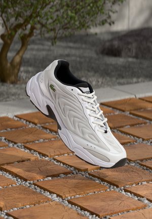 Scarpa sportiva bianca con tomaia testurizzata, caratterizzata da un interno nero, lacci stilizzati e un logo verde sul lato.
