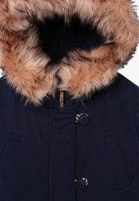 Abrigo de invierno azul marino con capucha forrada de piel sintética color beige, cremallera frontal, cierres de botón y dos bolsillos laterales.