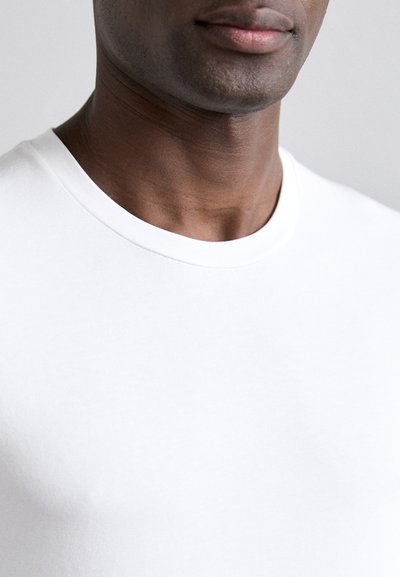 T-shirt bianca a girocollo realizzata in cotone leggero e morbido, con una forma aderente e un design minimalista. Senza pattern né accenti.