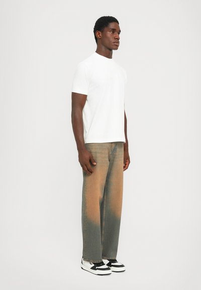 Vit kortärmad t-shirt, avslappnad passform. Bärs med högmidjade, urtvättade jeans i beige och grå toner, tillsammans med svart- och vitrandiga sneakers.