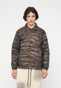 Gequilted pufferjack in bruin en zwart camouflagemotief, met een kraag, knoopsluiting aan de voorkant en elastische manchetten. Lichtgewicht stof.