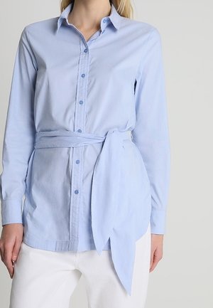 Camicia azzurro chiaro con maniche lunghe, fascia legata in vita e bottoni abbinati. Tessuto liscio con vestibilità strutturata.