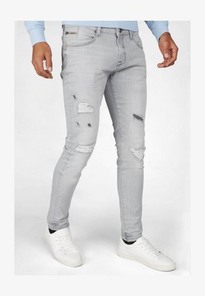 Jasnoszare obcisłe jeansy z przetarciami, w tym łatami i dziurami. Połączone z białymi trampkami, tworzą casualowy wygląd.