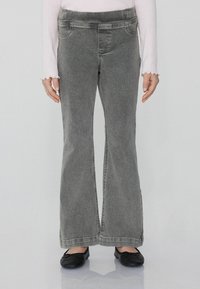 Szare dżinsy dzwony o wąskim kroju w talii, z przednimi kieszeniami i widocznym przeszyciem. Noszone z czarnymi balerinami.