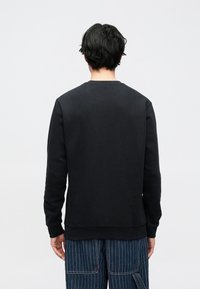 Fekete, kerek nyakú pulóver hosszú ujjakkal, bordázott mandzsettával és szegéllyel, valamint sima textúrával. Csíkos nadrággal viselve.