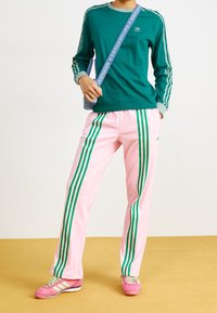 Grön långärmad skjorta med tre ränder, i kombination med rosa byxor med gröna ränder. Modellen har på sig rosa sneakers med gröna accenter.