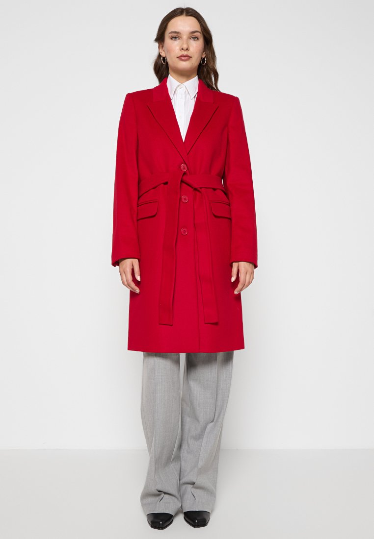 Cappotto rosso con colletto a rever, design doppiopetto e cintura. Presenta due tasche anteriori e una silhouette strutturata.