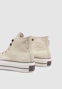 Zapatillas altas de cuero beige con detalles marrones, que cuentan con un logo redondo en el talón y suelas de goma blancas de contraste.