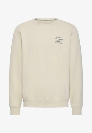 Bež jopica z okroglim izrezom, dolgimi rokavi in majhnim črnim logotipom besedila na levi strani prsnega koša z napisom "B.L.E.N.D The Best of the Denim Workers ESTD 1993".