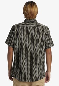 Camisa de manga corta con un patrón geométrico en blanco y negro, cuello abotonado, y tejido ligero con un corte relajado.