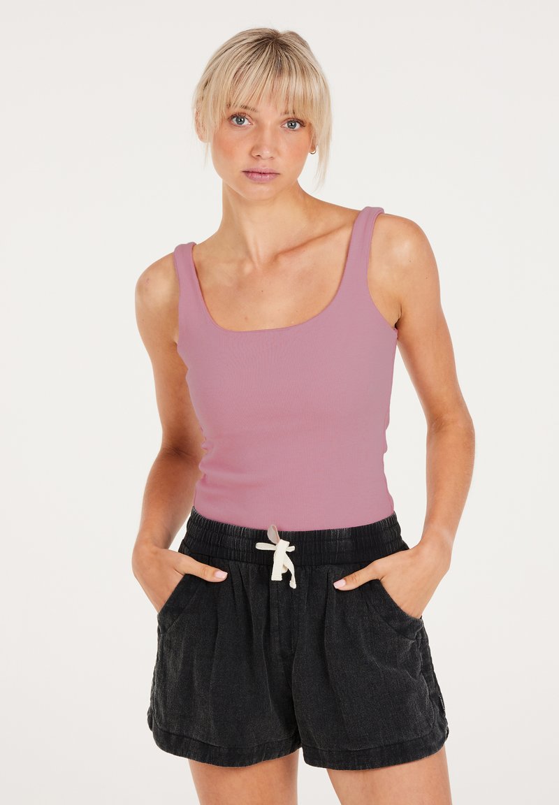 Lichtroze ribgebreide tanktop gecombineerd met zwarte shorts met trekkoord. De shorts hebben zakken en een losse pasvorm, wat een casual stijl benadrukt.