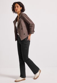 Veste brune courte à double boutonnage, jeans noir évasé et baskets blanches ; tissu lisse ; design structuré ; look décontracté.