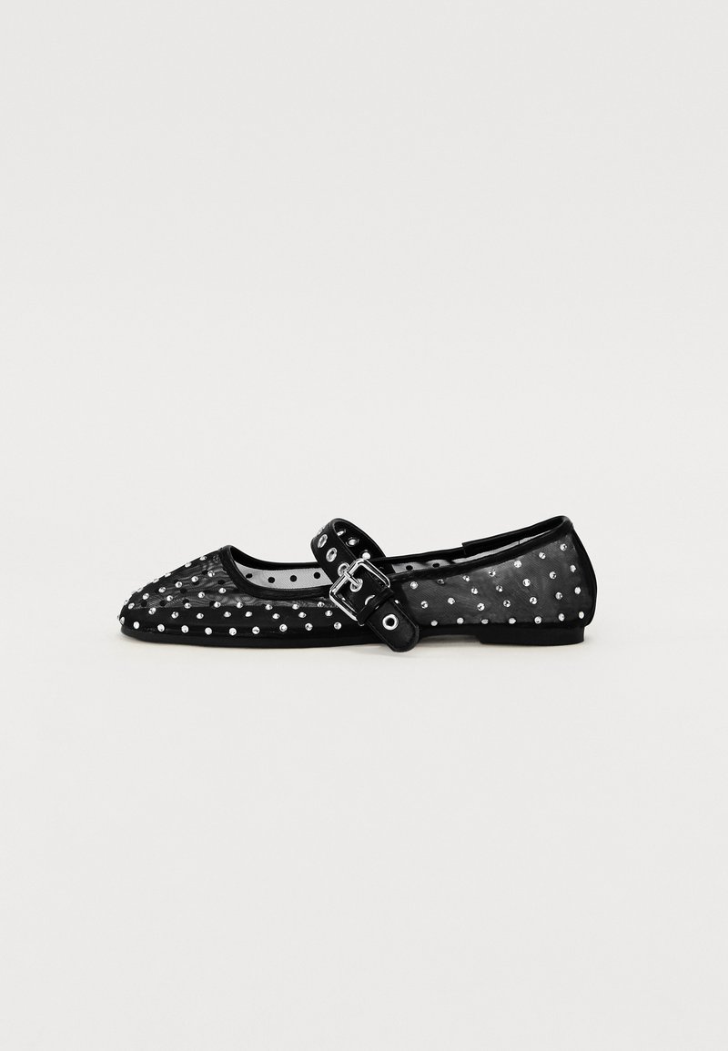 Chaussure plate noire transparente avec un bout pointu, ornée de clous en argent, dotée d'une sangle de cheville avec une boucle et d'une semelle plate.