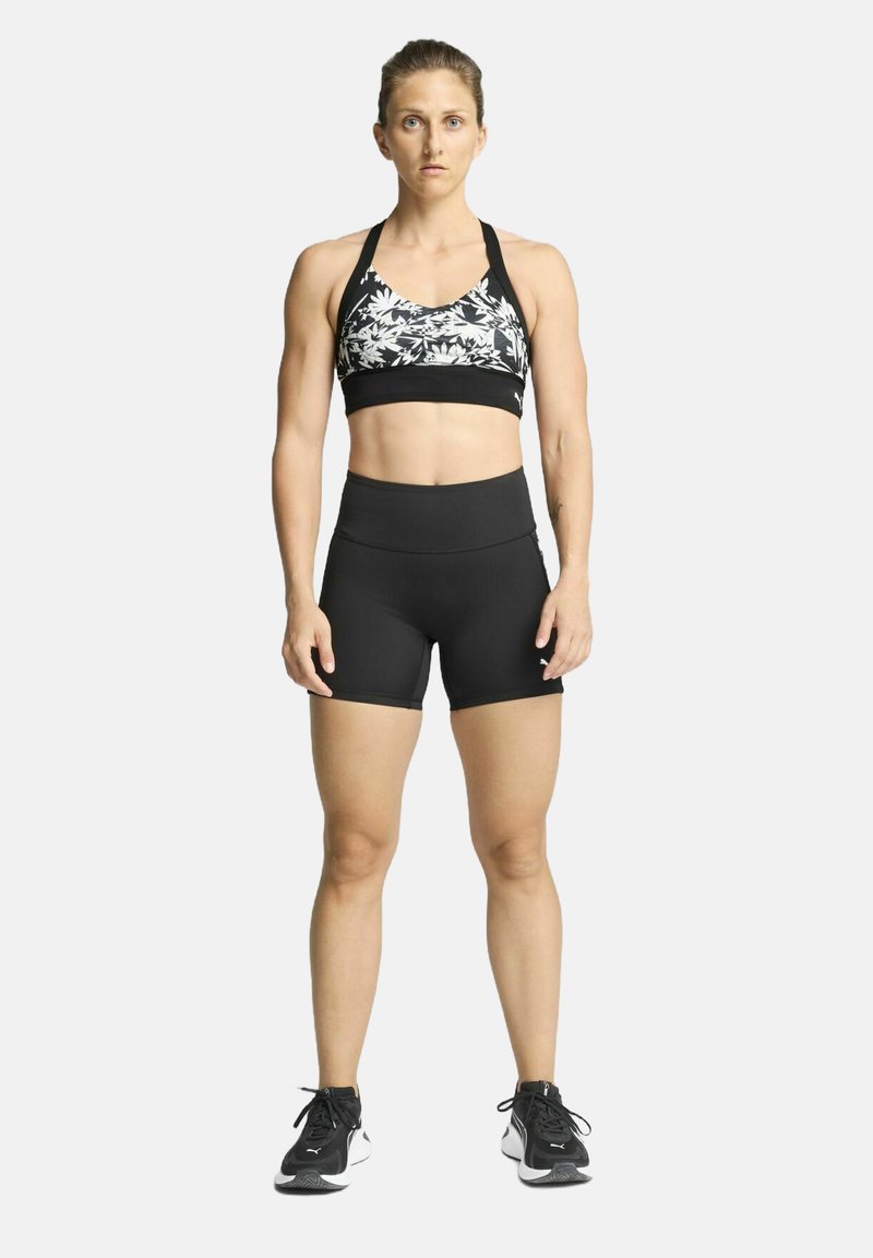 Soutien-gorge de sport avec un motif floral noir et blanc, associé à un short noir taille haute. Le modèle porte des chaussures de sport noires.