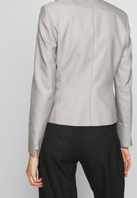 Blazer gris à carreaux avec une coupe ajustée, une texture de tissu lisse et des manches longues, associé à un pantalon noir.