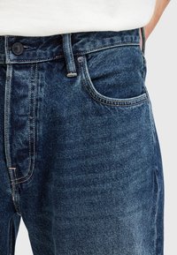 Jeans in denim blu scuro con un classico design a cinque tasche, caratterizzati da cuciture a contrasto, chiusura con bottone e leggera scoloritura sul davanti.