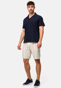 Chemise à manches courtes bleu marine à boutons associée à un short crème rayé et des baskets foncées, avec une coupe décontractée et un tissu doux.