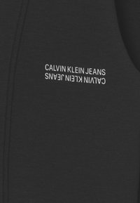 Schwarze Stoff-Hoodie mit "CALVIN KLEIN JEANS" in Weiß gestickt. Besitzt ein einfaches, lässiges Design und eine weiche Textur.