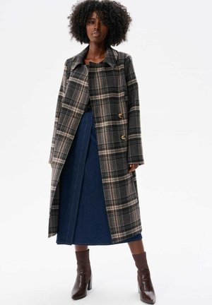 Plaid coat in black, brown, and cream, featuring a classic collar and two large gold buttons; paired with a denim skirt and brown boots.