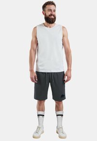 Mannen mouwloze witte tanktop gecombineerd met donkergrijze shorts met een berenontwerp, witte crew-sokken met zwarte accenten en witte sneakers.