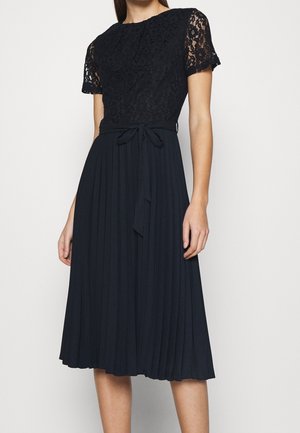 Robe marine avec un corsage en dentelle, des manches courtes et une jupe plissée. Équipée d'une ceinture à nouer et d'une texture de tissu lisse.