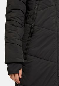Giacca a vento nera con motivo trapuntato, dotata di una cerniera laterale e polsini neri. Texture liscia con dettagli di fodera morbida.
