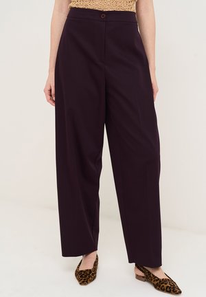 Kvinde iført mørkelilla bukser med høj talje og vide ben, kombineret med leopardmønstrede spidse slingback-flats, stående foran en ensfarvet baggrund.