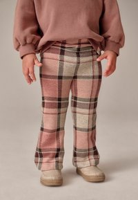 Vaaleanpunaiset ja beige ruudulliset housut, joissa on levenevä muotoilu ja pehmeä rakenne. Yhdistetty vaaleisiin mokkasiltaan.