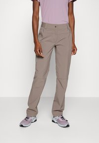 Lichte, beige buitenbroeken met een rechte pasvorm, ritszakken en een elastische tailleband. Gecombineerd met paarse sportschoenen.