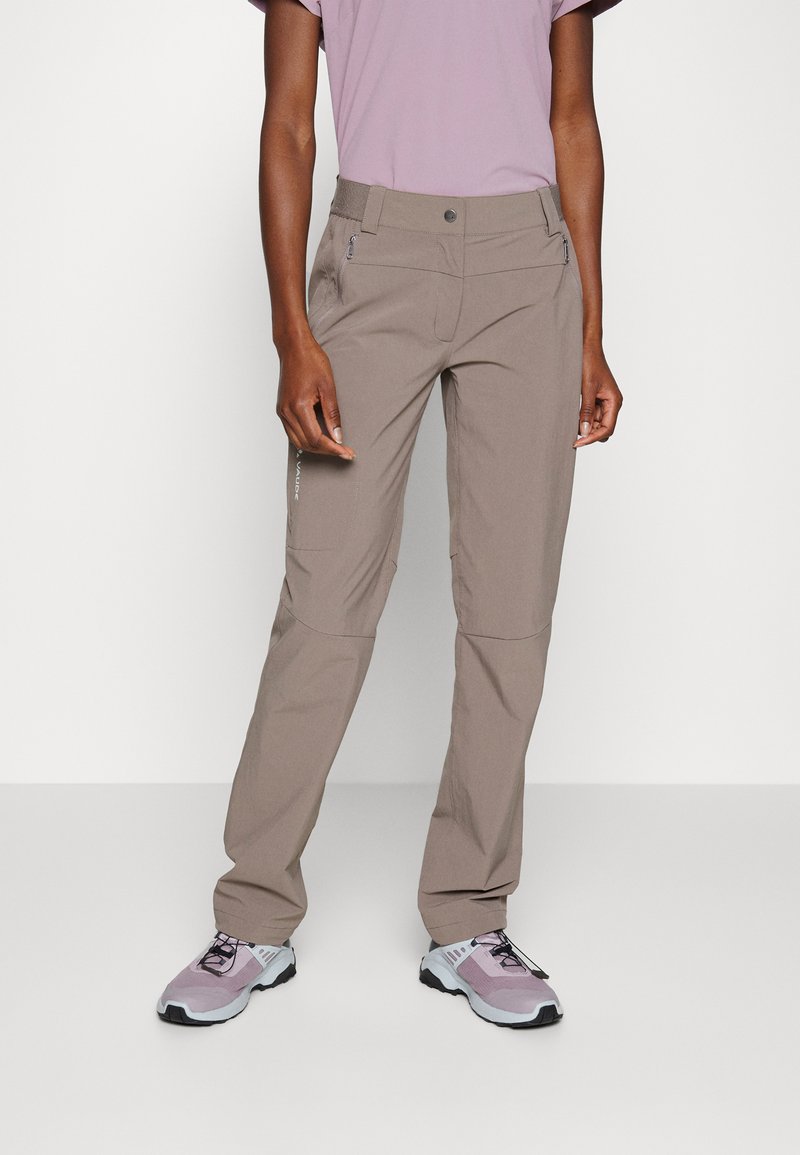 Lichte, beige buitenbroeken met een rechte pasvorm, ritszakken en een elastische tailleband. Gecombineerd met paarse sportschoenen.