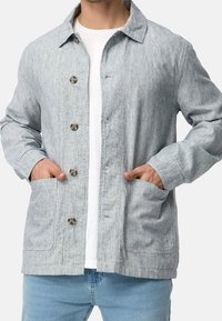 Light gray button-up jacket with a textured fabric, two front pockets, and a soft collar, worn over a white shirt and denim jeans.