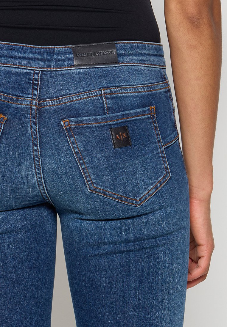 Niebieskie dżinsy z dopasowanym krojem, widocznym szwem oraz skórzaną metką z logo 'Armani Exchange' na pasku.