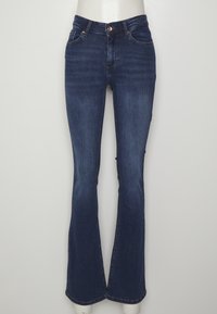 Jean en denim bleu foncé taille haute avec jambes légèrement évasées, bouton et fermeture éclair à l'avant, et cinq poches, présenté sur un mannequin.