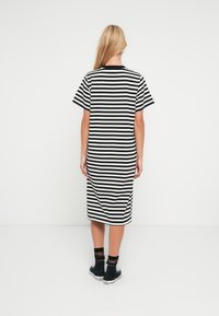 Φόρεμα με μαύρες και λευκές ρίγες, κοντά μανίκια και στρογγυλή λαιμόκοψη, που φτάνει ως τη μέση της γάμπας με χαλαρή εφαρμογή. Φοριέται με μαύρες μποτάκια αστραγάλου.