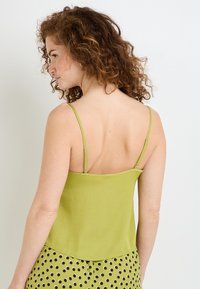 Top verde senza maniche con spalline sottili, texture liscia e design a taglio dritto. Il retro è semplice con uno stile minimalista, senza dettagli aggiuntivi.