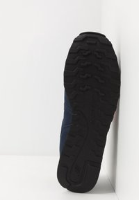 Námořnické modré sportovní boty s texturovanou černou gumovou podrážkou s cik-cak vzorem, lehkým textilním svrškem a značkovým logem New Balance.