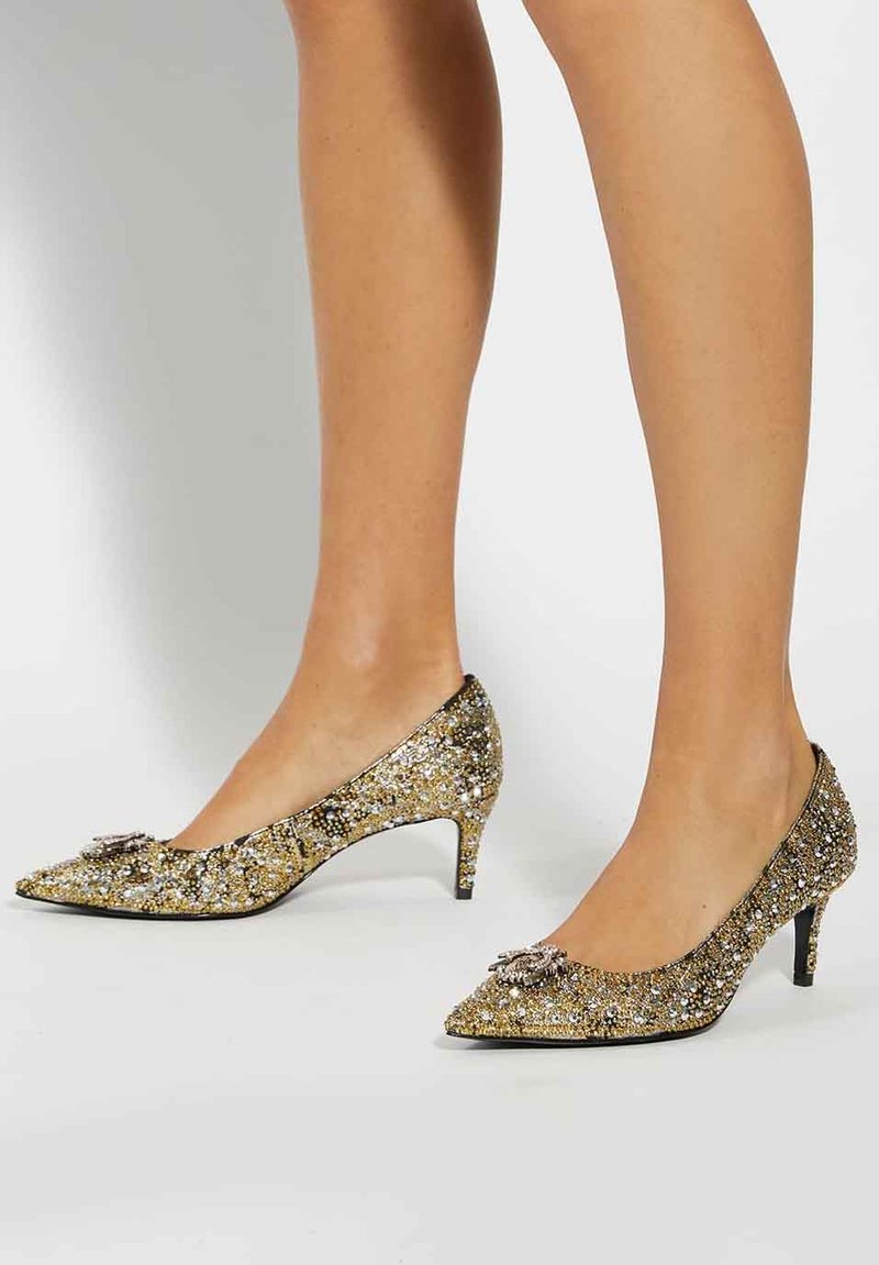 Gold glitter high-heeled pumps with pointed toes, featuring a decorative embellishment on the front and a textured finish on the upper.