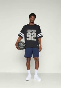 Fekete, oversized póló "Champion 92" nyomattal, tengerészkék sorttal, ami oldalán részletekkel rendelkezik, fehér sportzoknikkal és fehér tornacipőkkel párosítva.