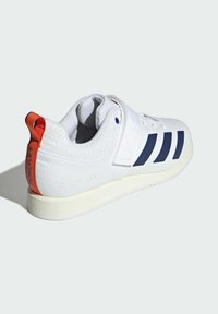 White athletic shoe with navy stripes, textured upper, velcro strap, and orange heel tab. Features a cream rubber outsole for traction.