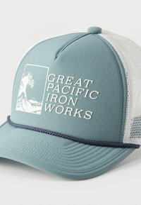 Ανοιχτό μπλε και λευκό καπέλο τύπου trucker με δίχτυ, με κείμενο «Great Pacific Iron Works» και λογότυπο κύματος στην μπροστινή πλευρά.